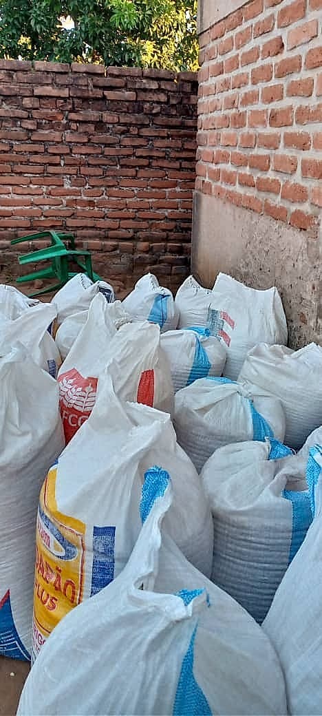 Large woven sacks filled with harvested crops are stacked against a brick wall in a storage area on the farm.